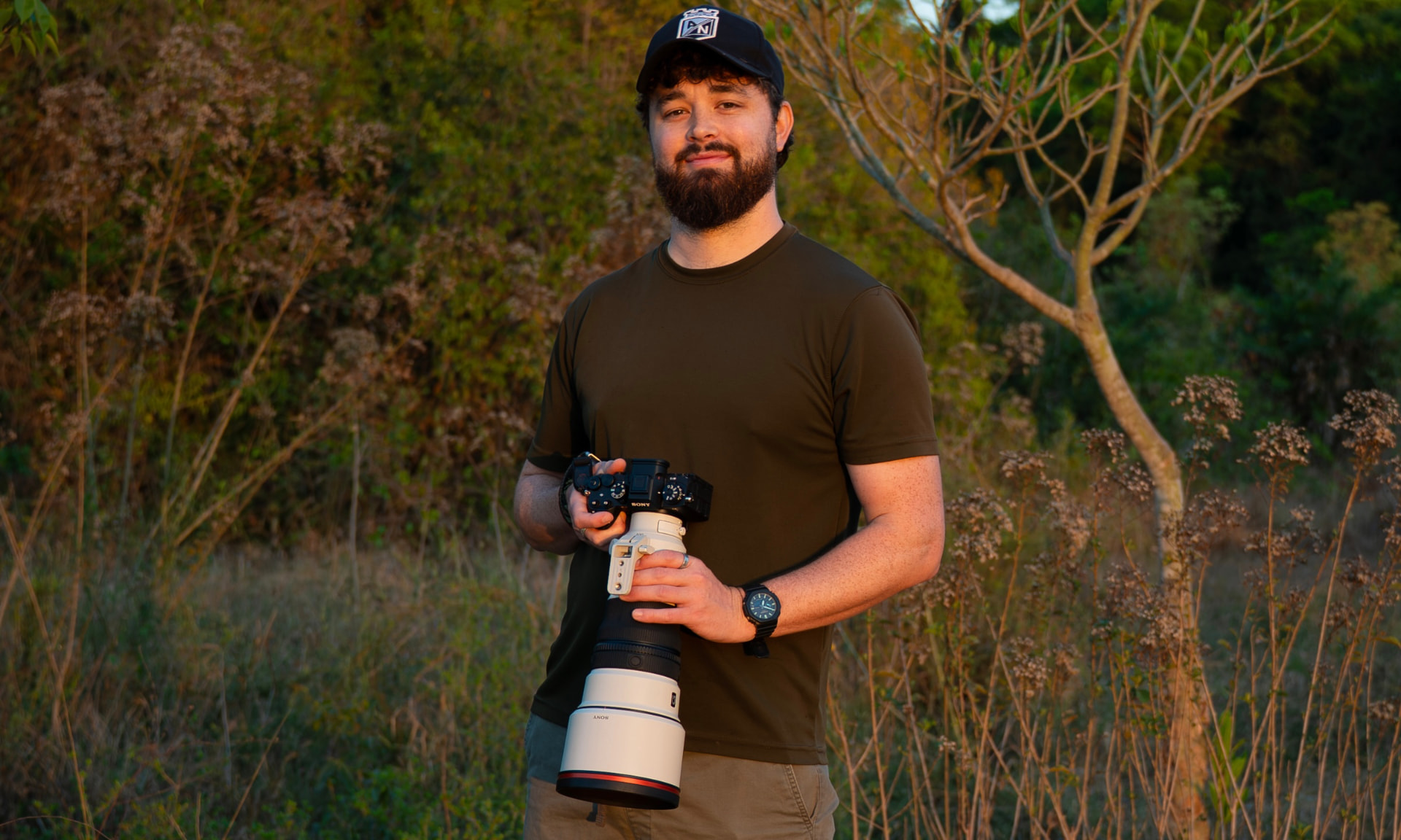 Charlie Page holding a camera with a large white telephoto lens in golden-hour light